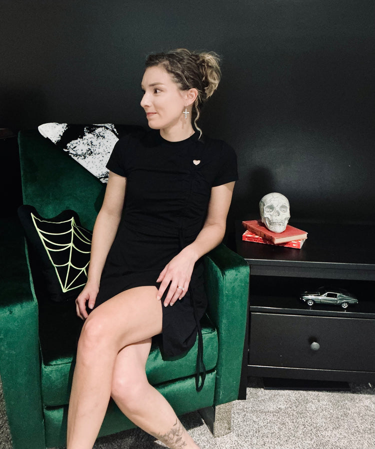 Woman in a black dress sitting on a green chair in a room with a black wall and decorative items.